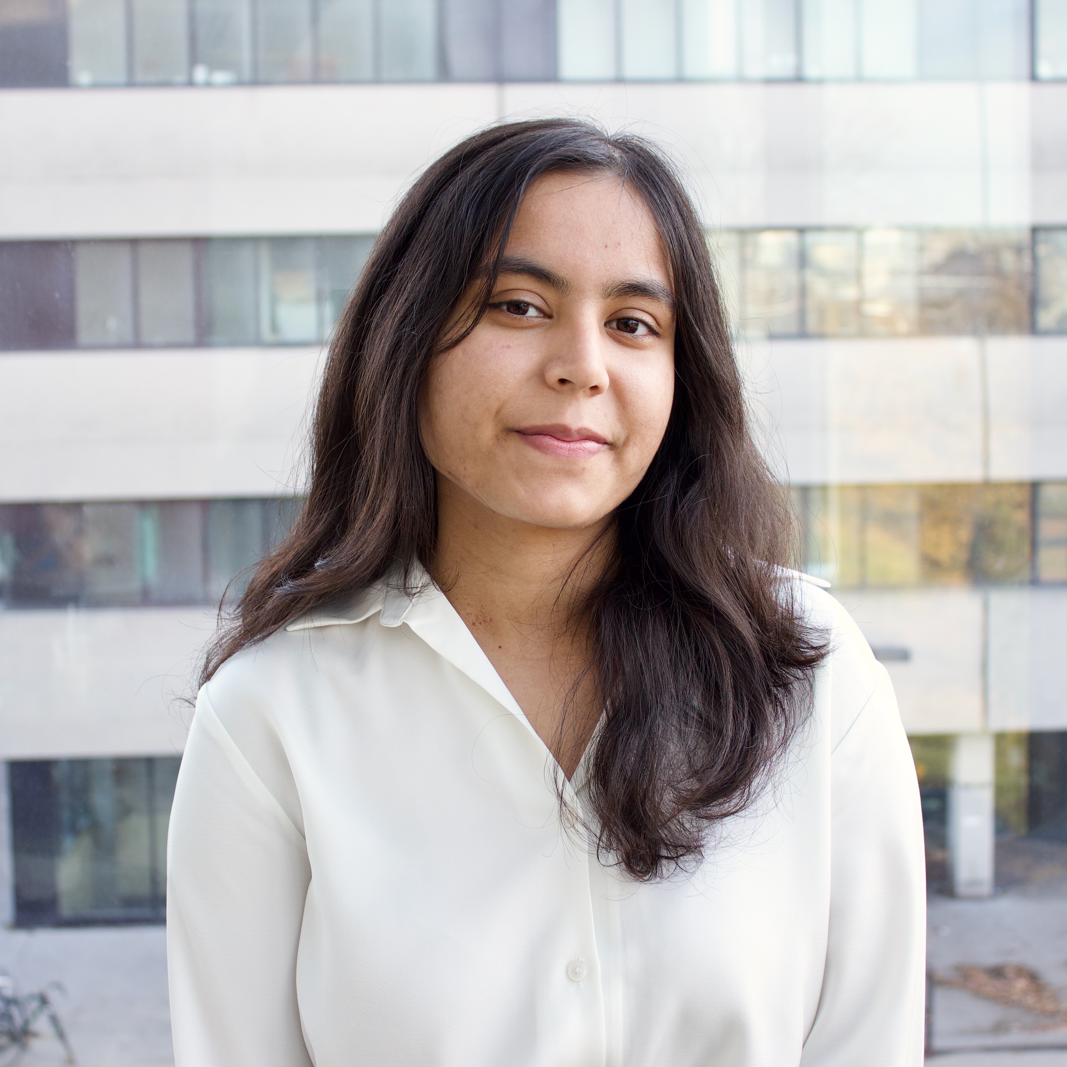 Sonia Persaud in front of a window,  wearing a white shirt and smiling.